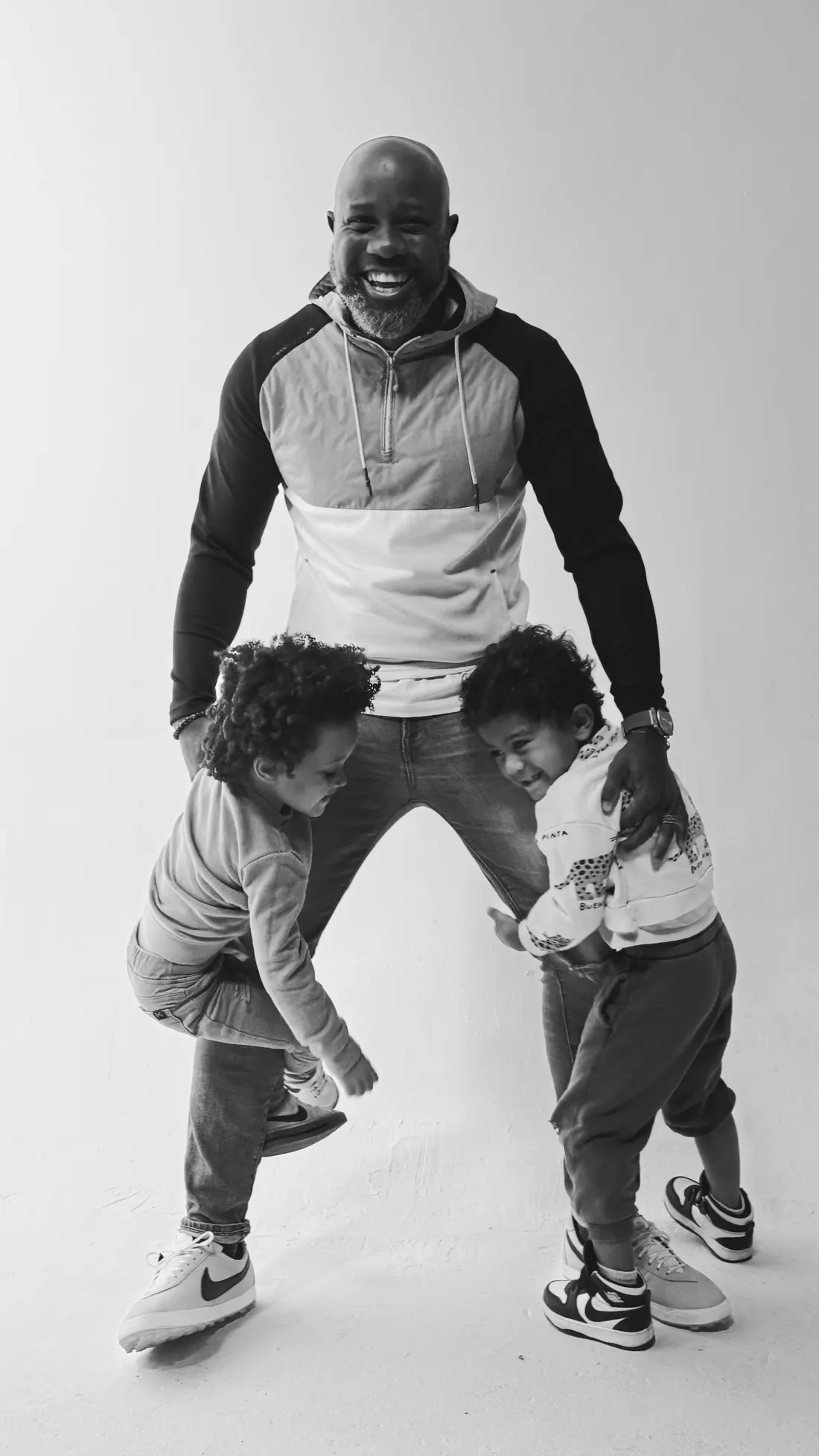 Hugo laughing in a studio portrait with his two young sons playing between his legs